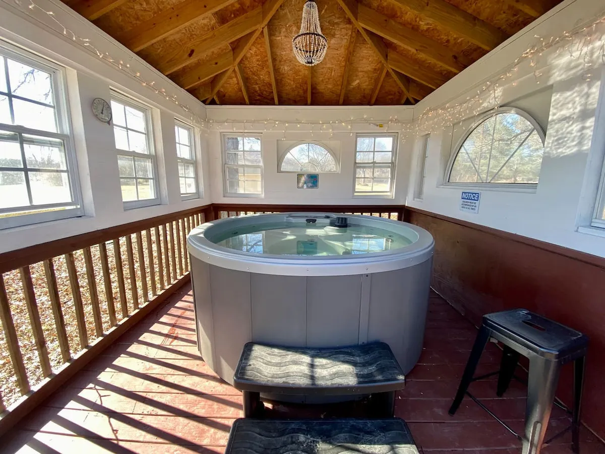 An inviting indoor hot tub surrounded by windows and a beautiful chandelier, set in a serene corner perfect for unwinding after a night on the town. The design suggests luxurious relaxation with views of the outdoors.