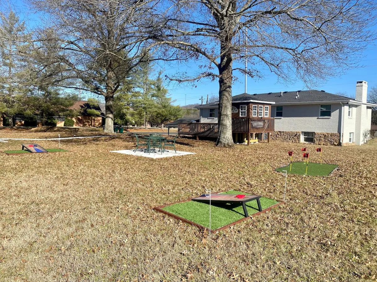 A cheerful exterior shot of the property’s expansive lawn, complete with lawn games set up, a picnic area, the deck of the house in view, and mature trees providing natural shade. The scene is lively and perfect for social gatherings or family competitions.