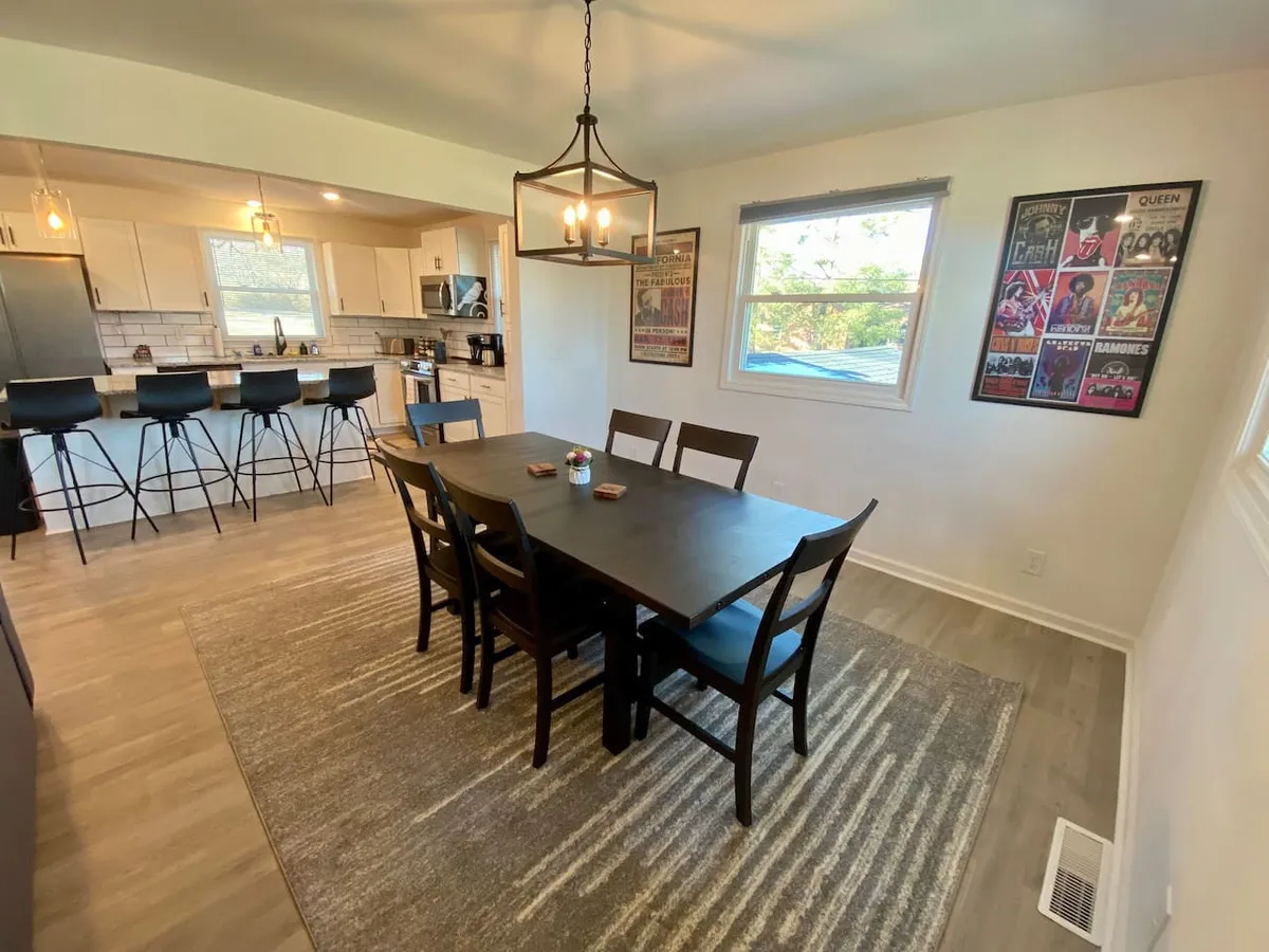 A stylish dining space with a modern table, chandelier overhead, tasteful artwork on the walls, and bar stools nearby. The setting is ideal for shared meals and lively conversation, merging elegance with friendliness.