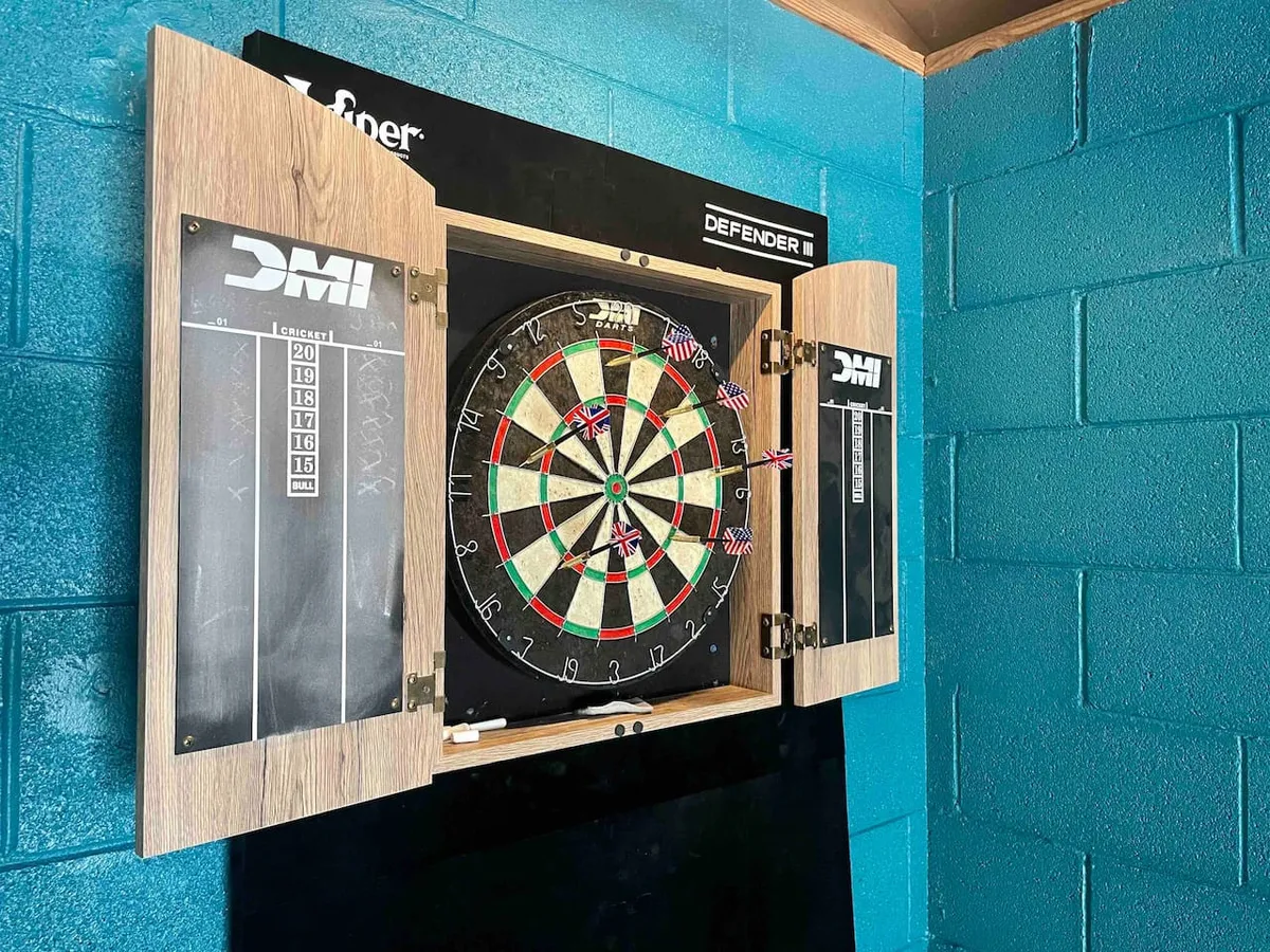 A cozy corner featuring a dart board and dart cabinet set against a colorful wall, ideal for focused dart matches and casual gatherings with friends. The setting exudes a sense of friendly competition and camaraderie.