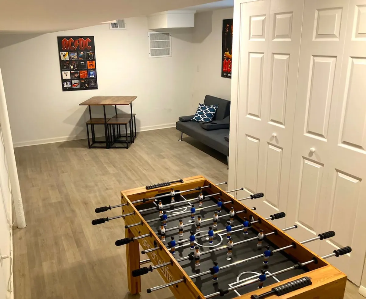 A lively interior game room with a foosball table, comfortable sofa, and art posters on the wall. The space is designed for playful interaction, relaxation, and group entertainment, offering an inviting setting for friendly competitions and casual hangouts.
