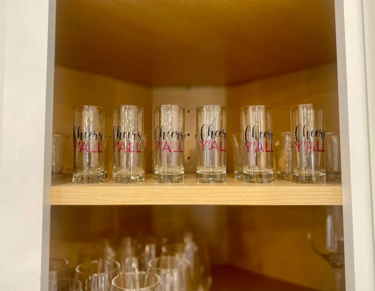 A shelf filled with glassware inscribed with 'Cheers Y'all', set against a warmly lit background. This image evokes celebrations, shared drinks, and joyful group moments, embodying the spirit of togetherness.