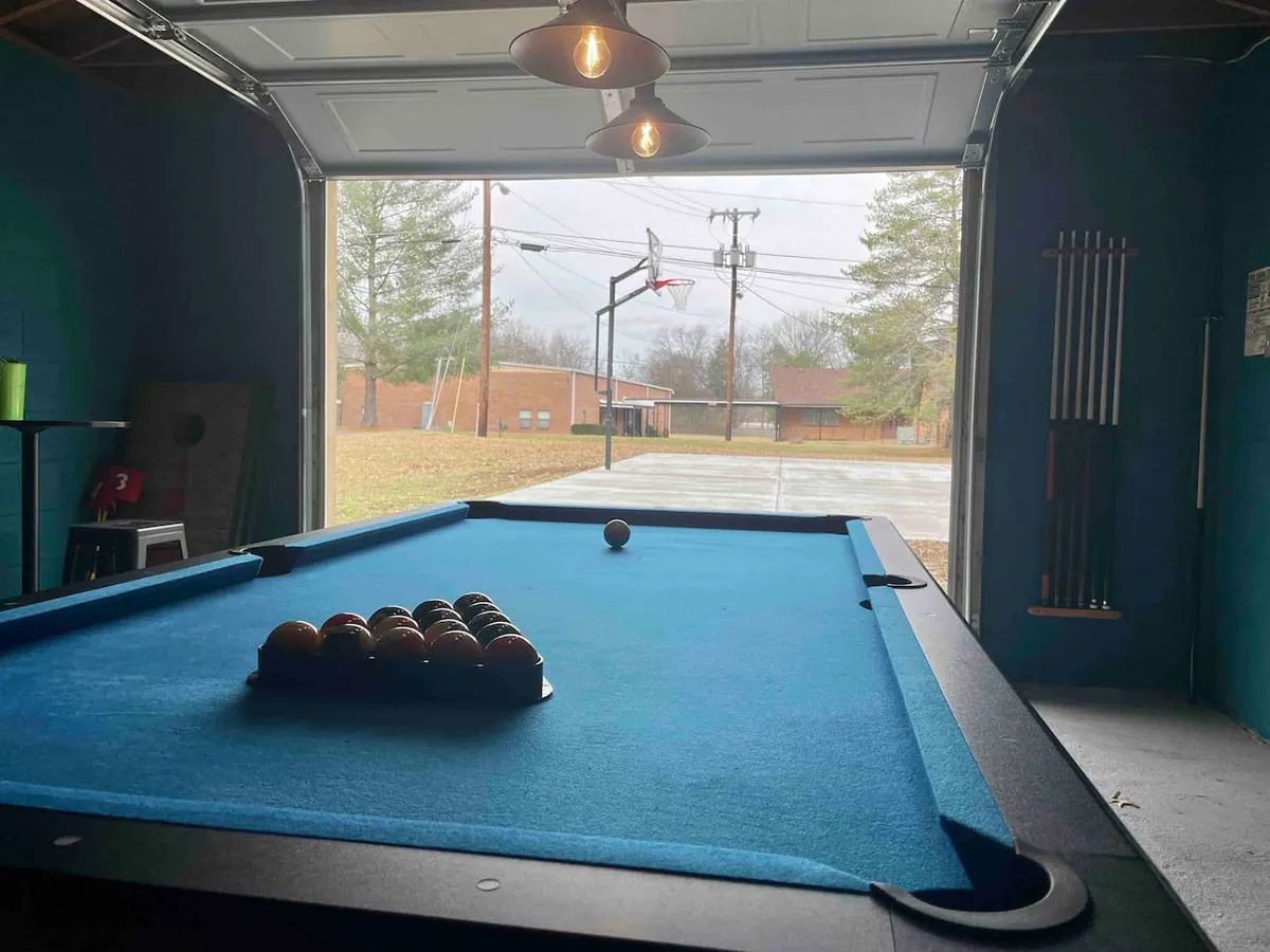 A game room featuring a pool table and open garage door leading to an outside basketball hoop, combining both indoor entertainment and a nod to outdoor connection. The relaxed atmosphere is ideal for late-night fun with friends after returning from the city.